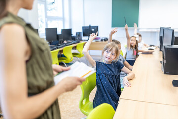 Students with hand raised looking at teacher standing in class at school