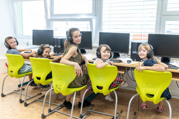 Smiling students with teacher wearing headphones sitting in computer class at school