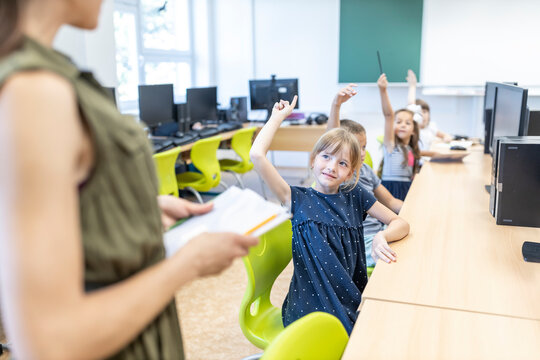 Students with hand raised looking at teacher standing in class at school