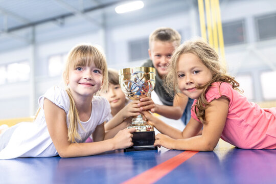 Smiling school students with trophy lying down at school sports court