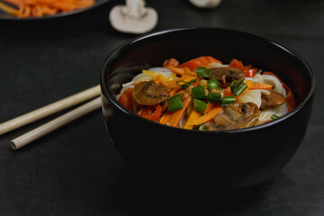 Asian noodles with vegetables on a dark background, champignon mushrooms and carrots