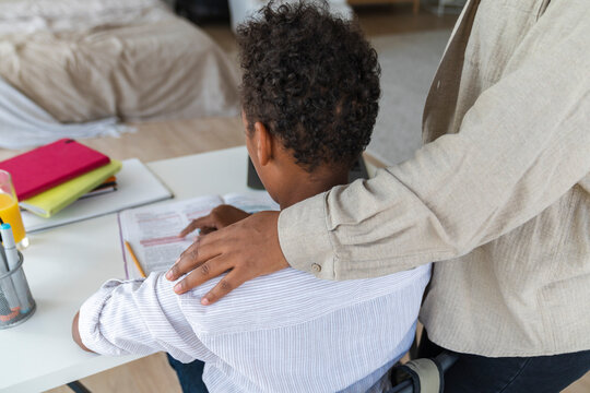 Mother standing by son studying at table in home