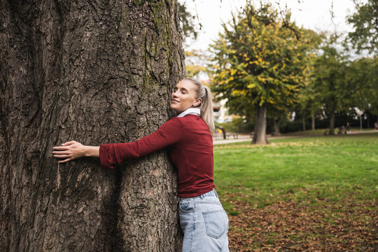 Smiling woman hugging tree at park