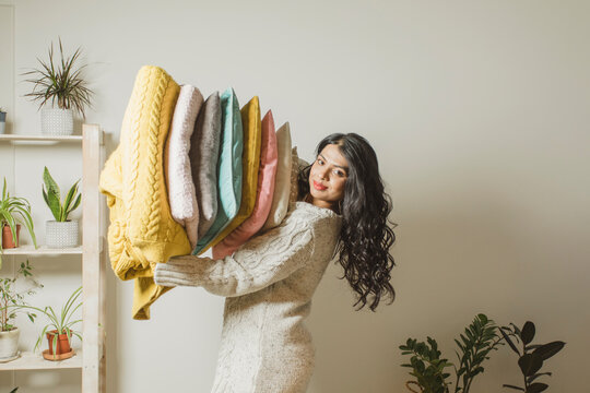 Smiling woman holding pillows and blankets at home