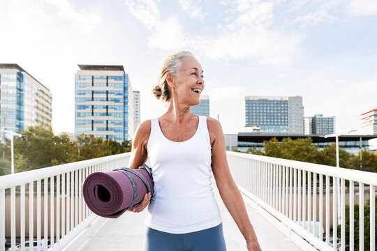 Happy woman with exercise mat on footbridge