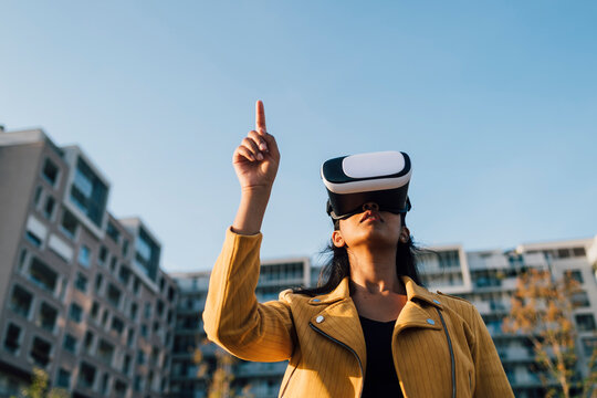 Young woman gesturing with virtual reality simulator under blue sky