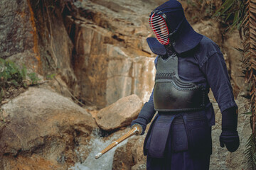 Portrait of kendoka man in a rocky background holding the sinai-sword.  Kendo is the Japanese martial art of sword fighting