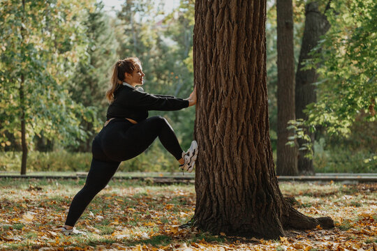 Smiling young woman exercising in front of tree at park