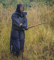 Full-length portrait of kendoka man in the forest holding the sinai-sword.  Kendo is the Japanese martial art of sword fighting