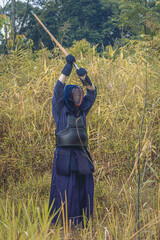 Full-length portrait of kendoka man in the forest raising the sinai-sword.  Kendo is the Japanese martial art of sword fighting