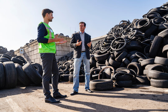 Businessman with colleague gesturing and discussing at recycling center - Powered by Adobe