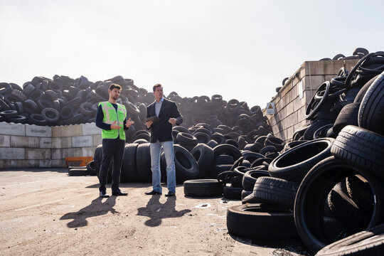 Businessman with colleague discussing over rubber tires at recycling center - Powered by Adobe