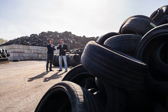 Businessmen discussing over heap of rubber tires at recycling plant - Powered by Adobe
