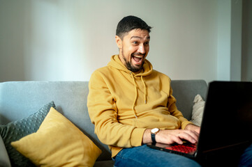 Excited man using laptop sitting on sofa at home