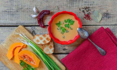 Fototapeta na wymiar Pumpkin soup on wooden table, linen cloth, vintage cutlery.