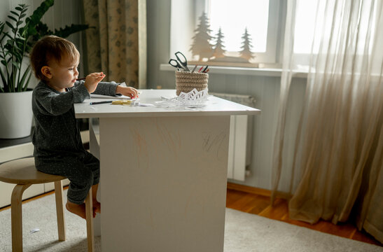 Baby boy sitting on stool near table at home