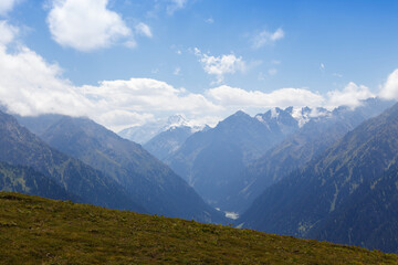 Mountain summer landscape. Snowy mountains and green grass. Peak Karakol Kyrgyzstan. Beautiful view from the top of the mountain