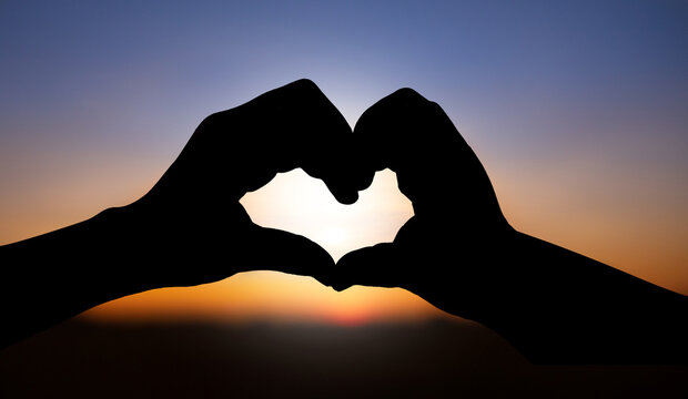 silhouette of love with hand heart shape over sunset sky background