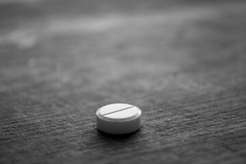 Black and white photo of the pill on the table. Round pill macro shooting on the table. On a wooden...