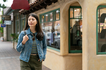 asian Korean woman traveler enjoying beautiful streetscape while taking relaxing walk past a retro building on the street in the town of Carmel in California usa