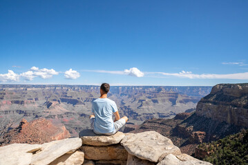 Fototapeta na wymiar Rear View Of Man Sitting On Viewpoint And Exploring Scenic Grand Canyon National Park During Sunny Day At Arizona