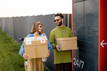 Man and woman carry parcels received in automatic post machine outdoors