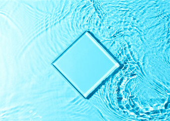 Mockup glass pedestal, glass stage lying in blue water with splashes. Top view, copy space.