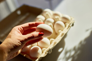 Woman hand take egg from cardboard box eggs on white background, hard sunlight, Organic egg pack product.