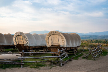 Covered wagons in yard at ranch with sky in background. Beautiful scenery of wrapped carts in...