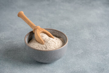 Psyllium husk in a bowl on a gray concrete background. Side view, selective focus.