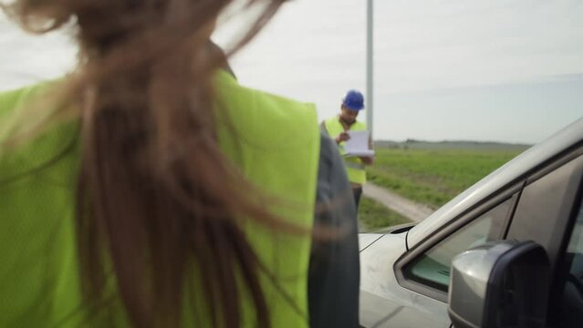 Caucasian woman came to field with windmill and talking with latin male engineer. Shot with RED helium camera in 8K.  