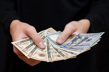 Different dollar bills in the hands of a young man in dark clothes, close-up.