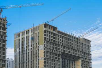 Fototapeta na wymiar Construction site. Construction cranes and a building under construction against a blue sky background. Construction cranes are working, walls of buildings are being erected.