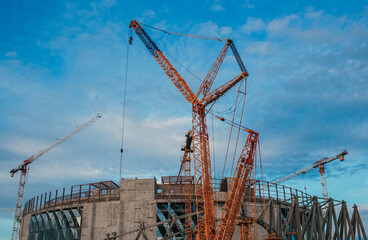 Fototapeta na wymiar Construction site. Construction cranes and a building under construction against a blue sky background. Construction cranes are working, walls of buildings are being erected.