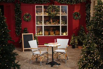 Table for two. Christmas cafe exterior with Christmas decorations and fresh bread in glass showcase. Cozy outdoor cafe on Christmas eve. Copy space. seasonal greetings concepts. Red walls