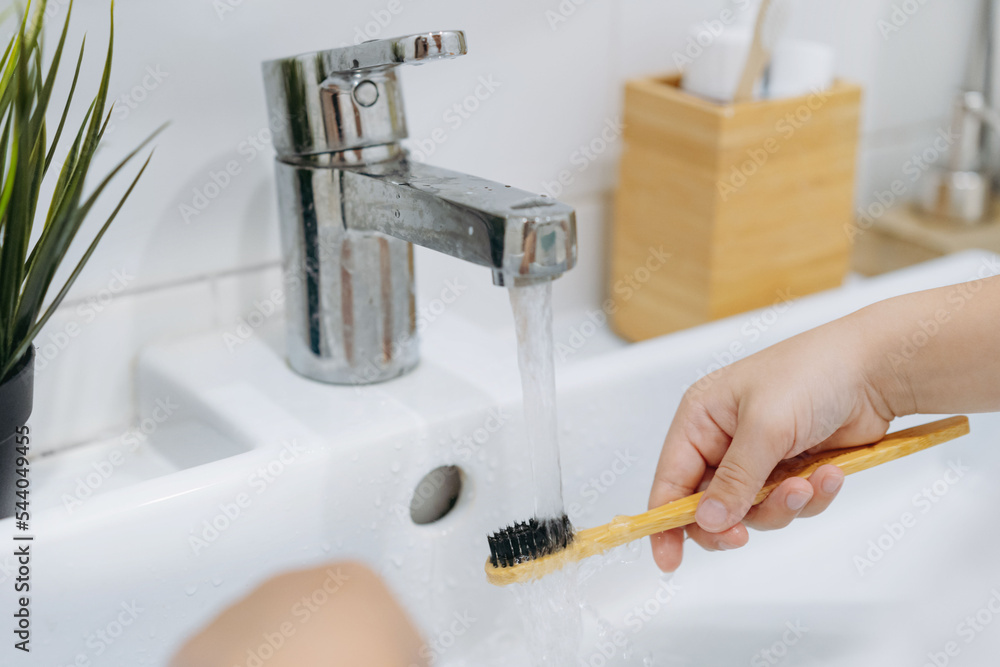 Wall mural child is rinsing bamboo tooth brus with water running from sink tap