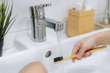 child is rinsing bamboo tooth brus with water running from sink tap - obrazy, fototapety, plakaty