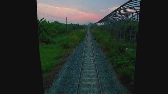 Travel by train in Thailand. View through the rear door of the car. The railroads going into the distance from the time of the red dawn. Asia Railway.