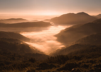 Fototapeta na wymiar Aerial view over the mountains filled with mist in the light of sunrise