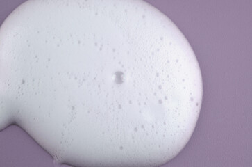 Macro photo of white shampoo foam on purple background