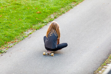 Mädchen sitzt auf Ihrem Skateboard und fährt auf einer Spielstraße