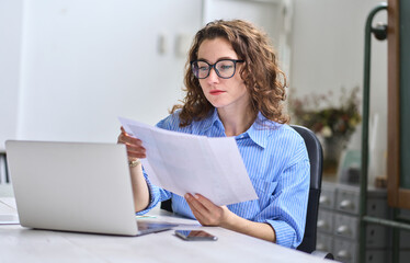 Young busy business woman manager, lawyer or company employee holding accounting bookkeeping documents checking financial data or marketing report working in office with laptop. Paperwork management - obrazy, fototapety, plakaty