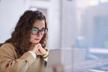 Young serious busy professional business woman employee or student wearing glasses using laptop...