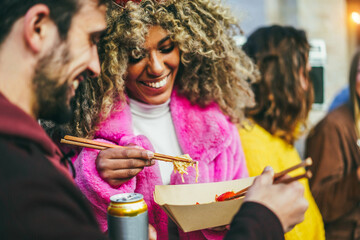 Multiracial young friends eating takeaway food outdoor - Focus on african girl chopsticks