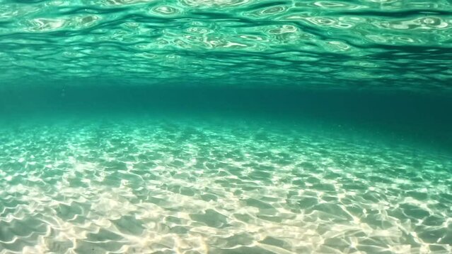 Sandy beach and sea bottom in sunny day. Rays of the sun make their way through the sea water forming bizarre patterns on the sandy bottom. Underwater shot, slow motion