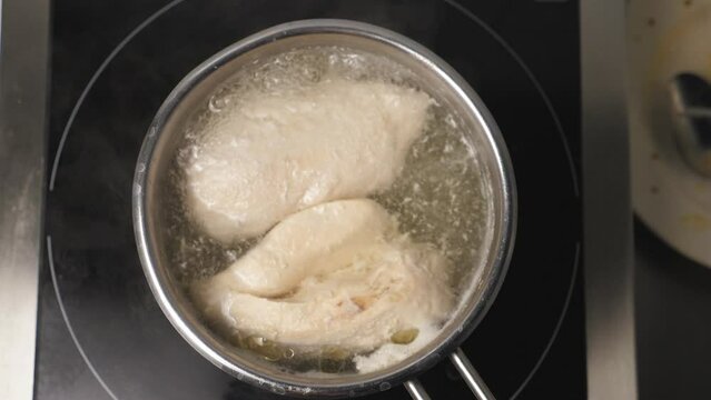 View of chicken breasts are boiling in a metal saucepan at kitchen restaurant. Chicken fillet is cooking in stewpan at cuisine. Concept of preparing meat. Top view Slow motion