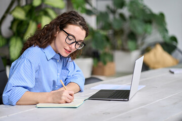 Young business woman worker using laptop writing notes, female employee sitting at desk in office...