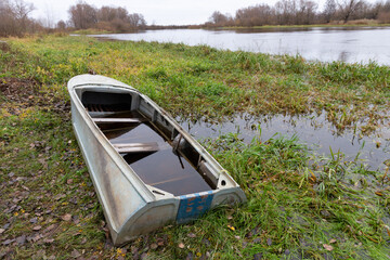A semi-submerged aluminum or duralumin boat on a swampy river bank. Autumn, October. november. Overcast weather