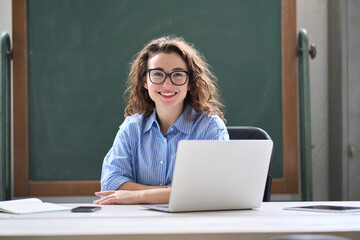 Young happy business woman sitting at work desk with laptop. Smiling school professional online teacher coach advertising virtual distance students classes teaching remote education training. Portrait - obrazy, fototapety, plakaty