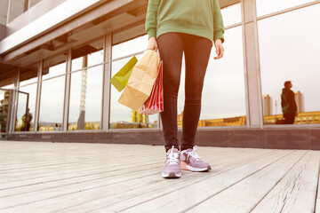 woman in black jeans and pink sneakers, with shopping bags, stands near the mall